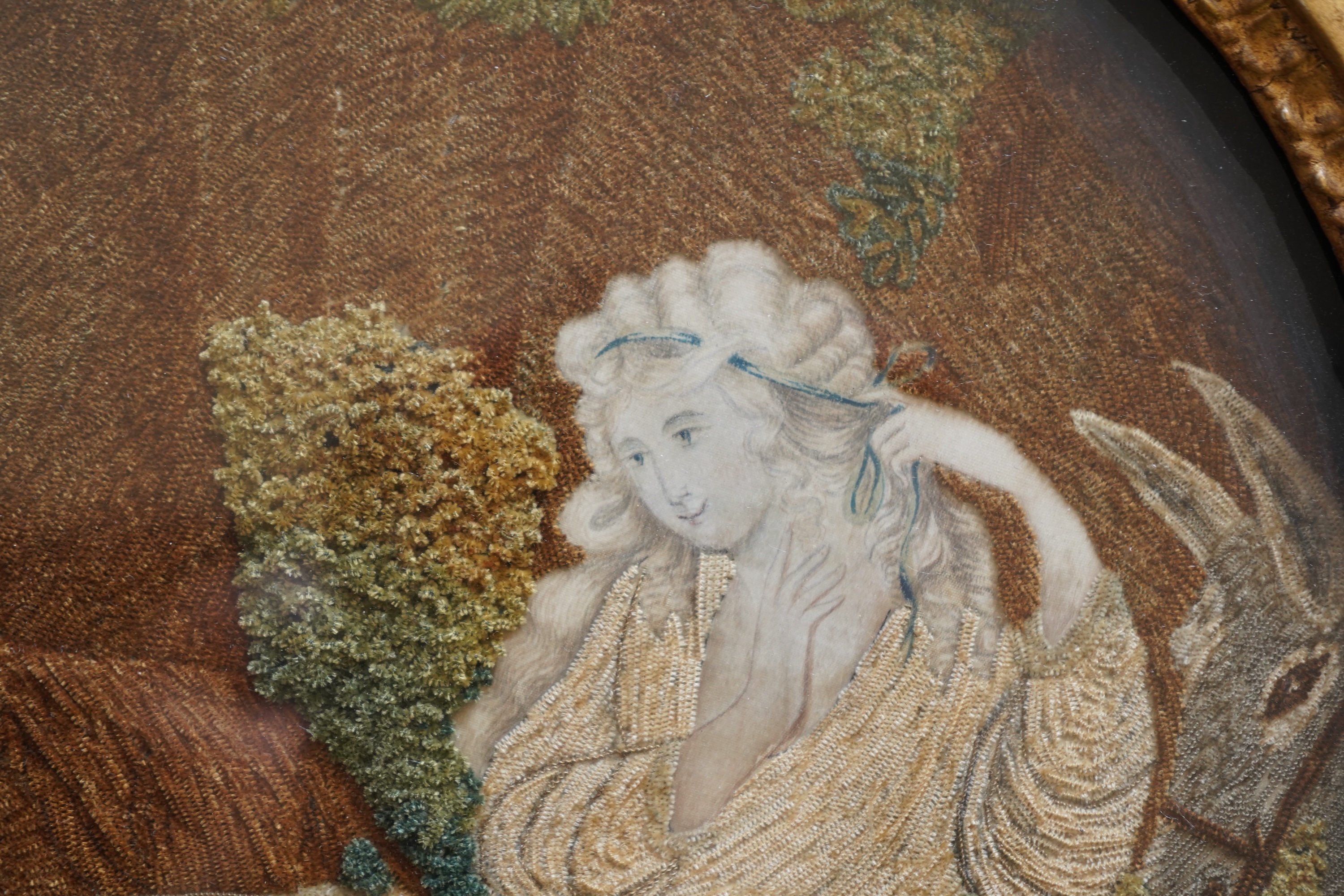A pair of unusual early 19th century oval silk Chenille embroideries, one depicting a seated lady surrounded by a lion and donkey, the other depicting a seated shepherdess under tree with two sheep. Both have water colou